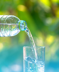 Drink water pouring in to glass over sunlight and natural green background.Water splash in glass Select focus blurred background.
