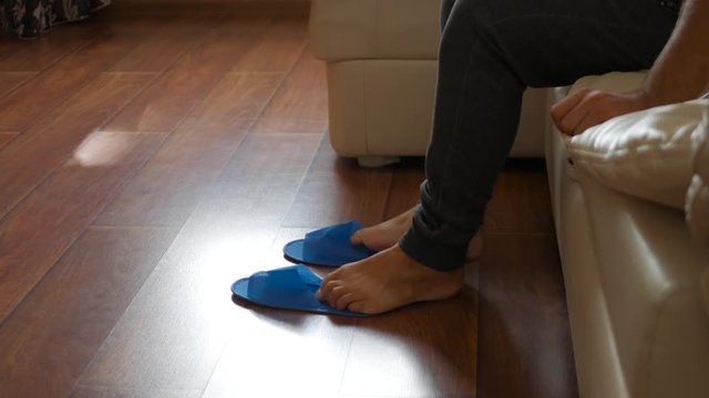 A man gets up at bed and wears disposable slippers at hotel.