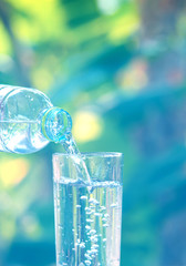 Drink water pouring in to glass over sunlight and natural green background.Water splash in glass Select focus blurred background.