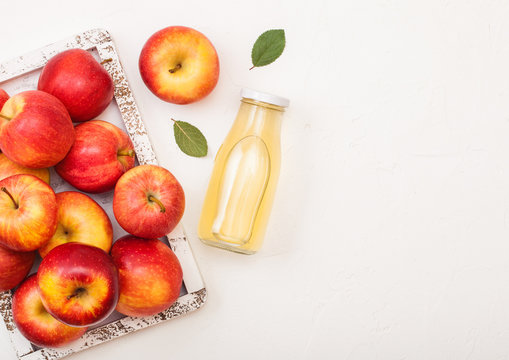 Glass bottle of fresh organic apple juice with red apples in vintage box on wooden background