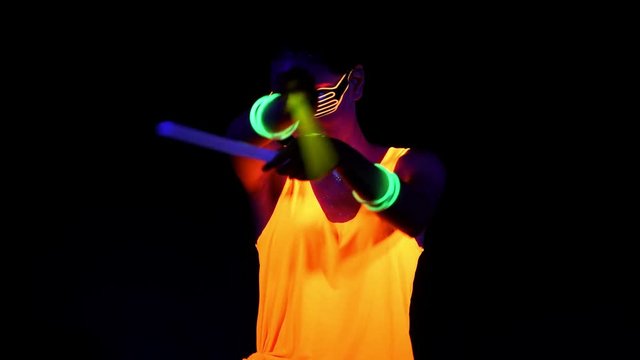 Beautiful sexy woman with UV face paint, glowing clothing, glowing glasses, bracelet dancing in front of camera holding chemical light, half body shot. Asian woman. Party concept.
