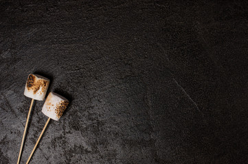 Roasted marshmallow on the sticks, black textured background