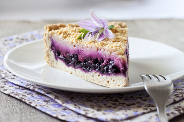 Piece of blueberry cake on a plate decorated with a purple flower
