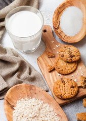 Fototapeta na wymiar Healthy organic oat cookies with chocolate with glass of milk on wooden board on stone kitchen table background. Sugar and raw oats in olive wooden bowl.