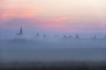 Church tower and village in fog at dawn