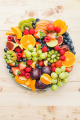 Healthy fruit platter, strawberries raspberries oranges plums apples kiwis grapes blueberries on the light wooden pine table, top view, copy space for text, selective focus