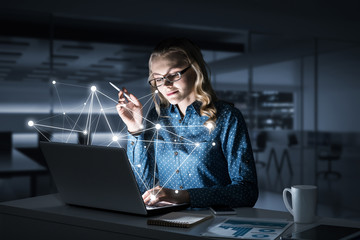 Attractive blonde wearing glasses in dark office using laptop. M