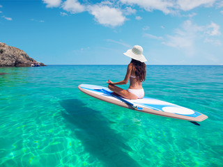 A beautiful young woman relaxes on a SUP board in the sea near the island. Standup paddleboarding...