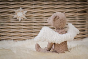 A teddy bear with angel wings sits on the background of a wicker basket. Blank form Kindness, hope,...