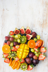 Fototapeta na wymiar Variety of cut fruits and berries platter, strawberries blueberries, mango orange, apple, grapes, kiwis on the white wood background, copy space for text, vertical, top view, selective focus