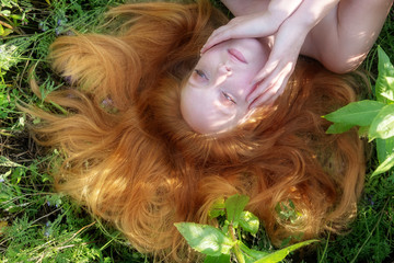 Schöne junge nachdenkliche sexy Frau, Portrait, die Augen halb geschlossen, liegt auf der grünen Wiese, mit Blumen, in der Natur, die feurigen roten Haare um das Gesicht drapiert