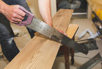 Man is sawing the wooden plank. Builder is working with a saw for renovation repairing works. Maintenance indoors in the flat.