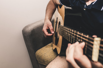 Man at home is playing the guitar. Guys hands are taking the chord on strings. Music making...