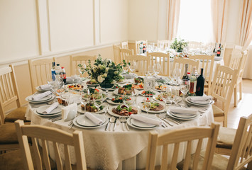 Beautifully set round tables at the restaurant. Delicious food at the wedding reception. White tablecloths and flowers decorations. Elegant space in the big hall. Happy celebration.