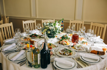 Beautifully set round tables at the restaurant. Delicious food at the wedding reception. White tablecloths and flowers decorations. Elegant space in the big hall. Happy celebration.