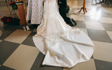Traditional wedding ceremony at church. Groom and bride with a long dress train are standing on the...