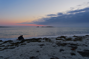 Fototapeta na wymiar On a beach in Brittany with the silhouettes of two young people watching the sunset.