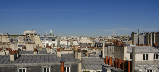 Fototapeta premium The roofs of Paris and its chimneys under a clouds sky