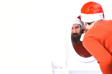 Santa Claus looks into mirror. Man with beard and hat