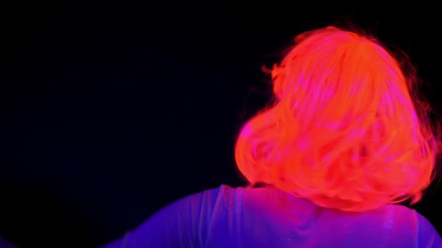 Beautiful sexy woman with UV cyborg face paint, wig, glowing clothing portrait dancing hard, back shot. Asian woman. Party concept.