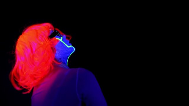 Beautiful sexy woman with UV cyborg face paint, wig, glowing clothing portrait dancing hard, side shot. Asian woman. Party concept.