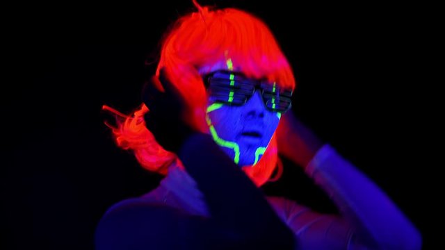 Beautiful sexy woman with UV cyborg face paint, wig, glowing clothing portrait dancing hard. Asian woman. Party concept.