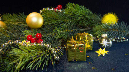 Merry Christmas & Happy New Year - fir (spruce) branch festively decorated: balls, garland, red berries, stars, with gifts wrapped in golden paper, against a dark blue background, selective focus