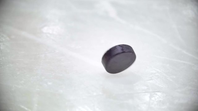 Black puck rotates on ice of ice hockey stadium. Slow motion