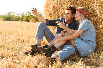 Naklejka na ściany i meble Happy young couple sitting at the wheat field