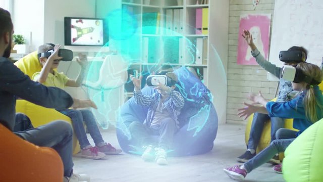 Playful little boys and girls sitting on colorful bean bag chairs, watching educational video in VR glasses and trying to touch holographic projection of Earth planet rotating in center of classroom