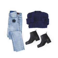 Jeans with star embroidery, blue knitted sweater and black leather ankle boots on white background. Overhead view of woman's casual day outfits. Trendy hipster look. Flat lay, top view.