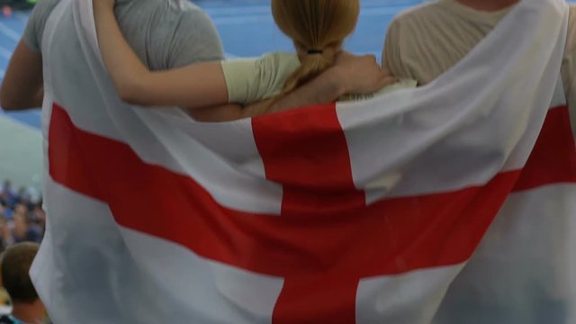 Sport fans with flag of England jumping at stadium, cheering team or sportsman