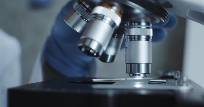 Close-up shot of sample slide and microscope with metal lens at laboratory.