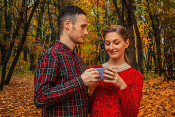 Couple in love holding cup of hot tea or coffee in autumn park