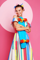 Fashion cool girl posing with a skateboard on pink background.