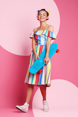 Fashion cool girl posing with a skateboard on pink background.