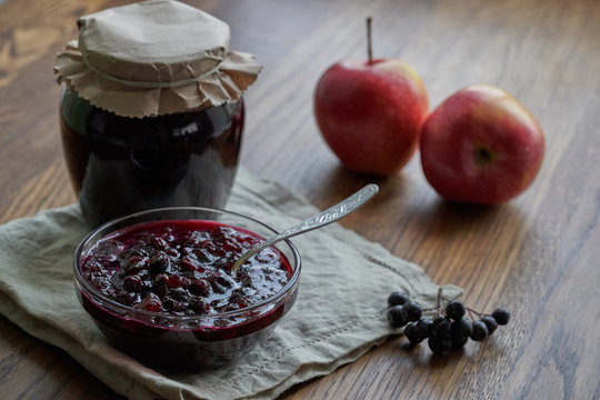Home made black chokeberry and apple confiture in a glass jar on a wooden background.