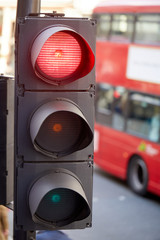 A U.K. traffic light, with the red stop light illuminated, with a London Bus in the background.
