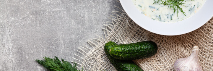 Panoramic copy space on a concrete table top with cucumber soup with sackcloth, garlic and jute material