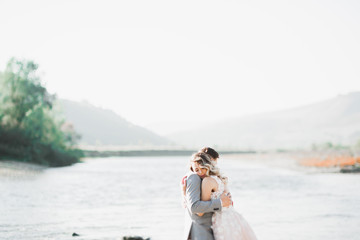 Elegant stylish happy blonde bride and gorgeous groom on the background of a beautiful river in the mountains