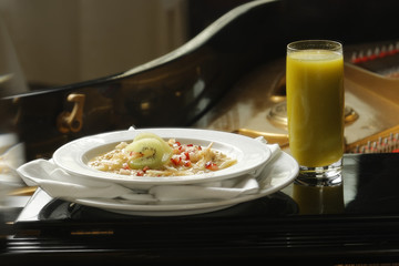 Breakfast of oat cereal with strawberry pieces with kiwi and green juice and in the background the interior of a piano.