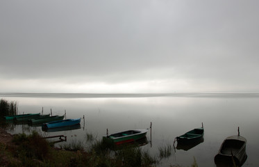 Foggy lake at sunrise with parked boats on it