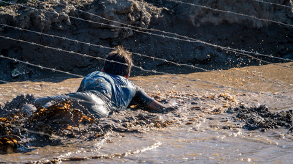 Athlete crawling under barbed wire in dirty mud, 
obstacle course race 