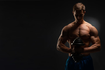 Fototapeta na wymiar Handsome power athletic man in training swap muscles with dumbbells. A strong six-pack bodybuilder, perfect abs, shoulders, biceps, triceps and chest. On a dark background under the banner