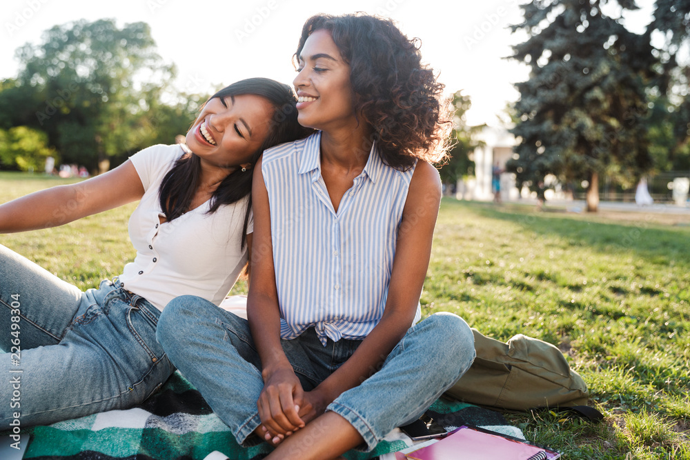 Poster Two cheerful young girls students sitting on a grass