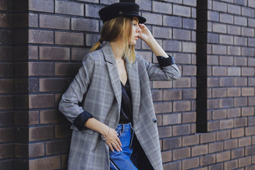 Young beautiful girl in a jacket, jeans and hat on a brick wall background