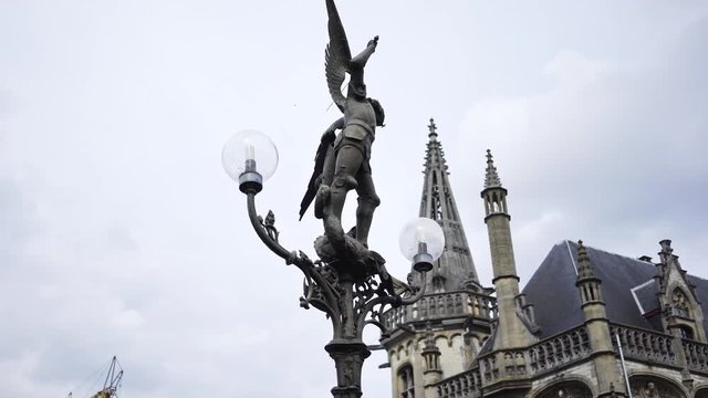 Old city centre of Ghent. Panoram around lantern in vintage style with sculpture of saint George at grey sky background. Street light of St. Michael Bridge