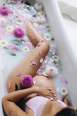 Look from above at beautiful pregnant woman in pink lingerie lying in a bath full of pink flowers and milk