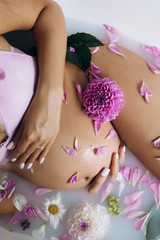 Look from above at beautiful pregnant woman in pink lingerie lying in a bath full of pink flowers and milk