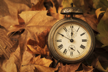 closeup of an old and rusty alarm clock surrounded by dry leaves, depicting the end of the summer...